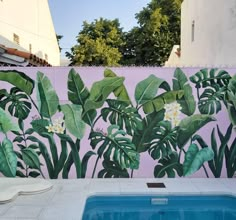 an outdoor swimming pool in front of a painted wall with tropical leaves and flowers on it