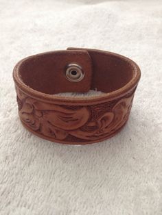 "This wrist band is made from heavy vegetable tanned cowhide with heavy duty snaps for years of wear. It is 1-1/4 \" wide and made to fit your wrist. The band is stained and a protective finish is used to add extra life. The edges have been hand rubbed to a super smooth finish that won't irritate you. To get your correct size measure around your wrist with a flexible tape measure or use a string and measure string with a ruler." Western Hand Tooled Leather Bracelet, Tan Cowhide, Wrist Band, Hand Tooled Leather, Bolo Tie, Tooled Leather, San Antonio Tx, Tape Measure, Leather Tooling