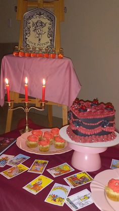 a table topped with cupcakes and cards on top of a purple table cloth