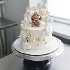 a white cake with gold stars and a teddy bear sitting on the top one tier