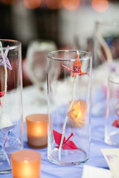 several vases filled with flowers and candles on top of a blue cloth covered table