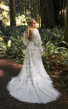 a woman standing in the woods wearing a wedding dress with long sleeves and an open back