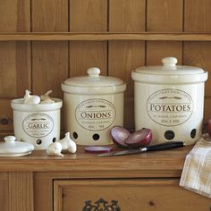 three white canisters sitting on top of a wooden counter next to garlic and onions