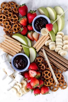 fruit and pretzels arranged on a platter with strawberries, apples, bananas, cinnamon sticks