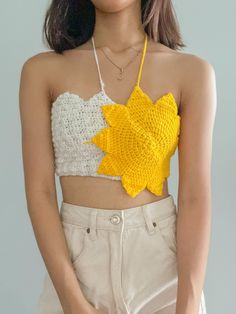 a woman wearing a yellow and white crop top with a crocheted flower on it