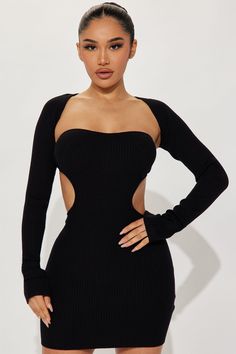 a woman wearing a black dress with long sleeves and cutouts on the sides, standing in front of a white background