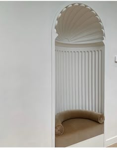 a white room with an arched window and beige cushion on the bench in front of it