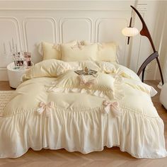 a white bed with ruffles and pillows on it in a room next to a lamp