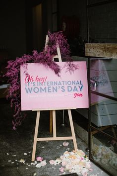 a pink sign that says international women's day with flowers on the ground next to it