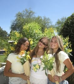 three beautiful young women standing next to each other holding bouquets of flowers in their hands