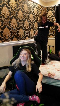 two women sitting on the floor in front of a bed and another woman standing up