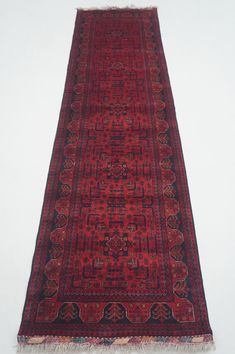 a red rug with black border and fringes on the bottom is laying against a white wall