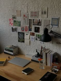 a wooden desk topped with a laptop computer next to a wall covered in pictures and books