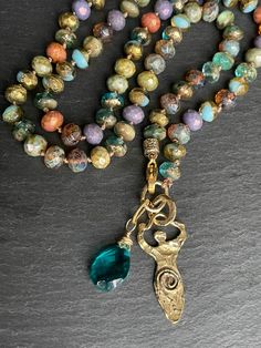 Boho goddess necklace; Boho Summer necklace;  Czech glass necklace; Artisan necklace; Long necklace; Summer; Bronze;  This one of a kind long necklace is made of czech glass beads with beautiful hues and sparkle. Necklace is hand knotted and a beautiful bronze goddess along with a chalcedony gemstone is used as focal. Necklace is approx 24 inches long. Please Note: I do my best to capture colors accurately on camera, however due to lighting and screen settings, colors may vary in person. Glass Beaded Necklaces With 108 Beads As A Gift, Bohemian Czech Glass Bronze Necklace, Bohemian Handmade Glass Necklaces, Spiritual Necklaces With Round Beads And Lobster Clasp, Unique Glass Pendant Necklaces, Handmade Gold Goddess Necklaces, Glass Pendant Necklace With Lobster Clasp, Handmade Goddess Pendant Necklace, Handmade Gold Goddess Necklace