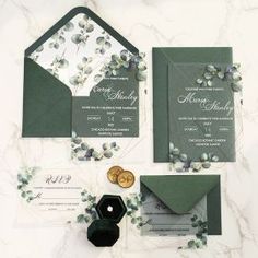 the wedding stationery is laid out on top of the marble table and features greenery