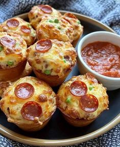 mini pizzas with pepperoni and cheese are on a plate next to a small bowl of sauce