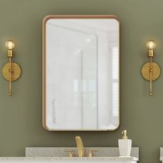 a bathroom vanity with a large mirror and two lights on the wall above it, along with gold faucets