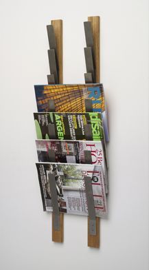 a magazine rack is mounted to the wall with two wooden pegs and holds magazines