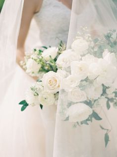 two brides holding bouquets of white roses and greenery on their wedding day