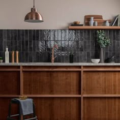 a kitchen with wooden cabinets and black tile backsplashing, copper pendant light over the sink