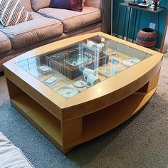 a coffee table with glass top on carpeted floor next to couches and pillows