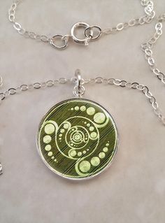 a green and white pendant with circles on it's back side, hanging from a silver chain