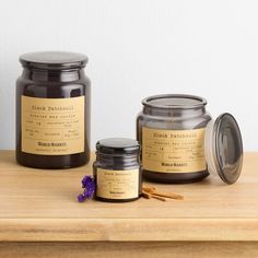 three jars of candles sitting on top of a wooden table next to some flowers and cinnamon sticks