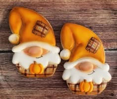 two decorated cookies sitting on top of a wooden table with white frosting and orange decorations