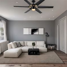 a living room with gray walls and white couches, black coffee table and ceiling fan