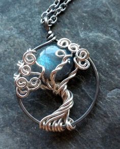 a tree of life pendant with a blue stone in the center on a black rock