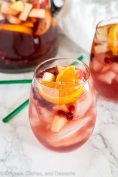 two glasses filled with fruit and ice sitting on a table next to another glass full of liquid