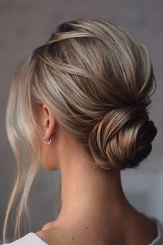 a woman with blonde hair styled into a low bun, wearing a white shirt and earrings