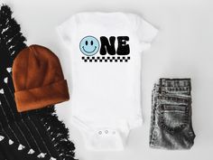 a white onesie with the word one on it next to jeans and a hat