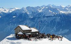 a group of people standing on top of a snow covered slope next to a building