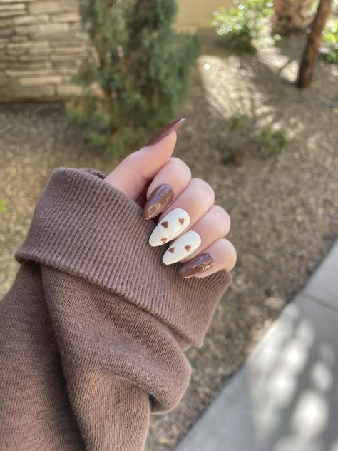 Chocolate brown nails with two white accent nails with small brown hearts 🤎 #nails #nailart #brownnails #brownaesthetic #heartnailart #heartdesign #heartnails #trendynailart #nailinspo #nailideas #almondnails #gelnails #gelpolish #gelextenstion Brown Nails Design Almond Shape, Brown Nails Thanksgiving, Brown Hearts Nails, Chocolate Nails Design Art Ideas, Brown Spooky Nails, Brown Coquette Nails, Mocha Mouse Nails, Coffee Themed Nails, Cream Brown Nails