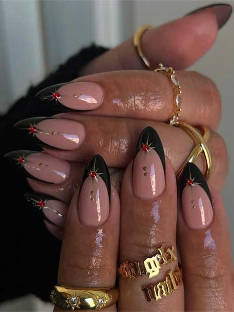 Black French tip nails on a nude base, adorned with gold stars and red rhinestones, featuring gold dots on the nude area. French Tip Nails With Design Rhinestones, French Tip Color Acrylic Nails, Black Nail With Red French Tip, Dark Gold Nails, Black French With Stars, Black Nails New Year, French Nails Acrylic Designs, Dark Red Gold Nails, Black French Tip Nails Designs