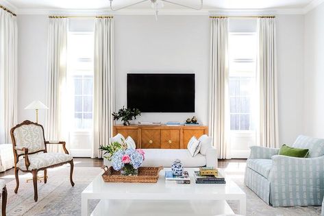 White curtains hang from brass curtain rods in front of windows flanking wooden TV console located beneath a wall mount TV. Tv Between Windows, Ideas Of Living Room, Windows Design Ideas, Brown Wooden Bed, White Settee, Wooden Tv Console, Brass Curtain Rods, Wall Mount Tv, Windows Design