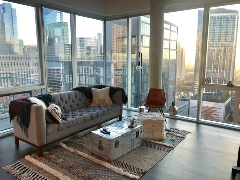 Modern living room with floor to ceiling windows, hardwood floors, concrete ceilings, grey suede couch, shag ottoman, metal trunk coffee table, red leather lounge chair, white fur throw pillows, and city views | Domu Chicago Apartments Grey Suede Couch, Floor To Ceiling Windows Apartment, White Fur Throw, Boujee Bedroom Ideas, Apartamento New York, Suede Couch, City Apartment Decor, Living Room Wallpaper Ideas, Chicago Apartments