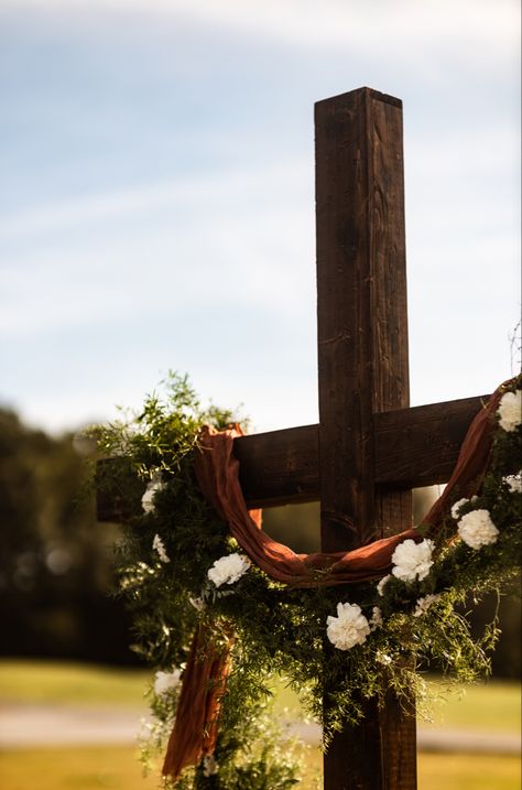 Beautiful cross with terracotta cheese cloth, greenery garland and white floral accents Cross Arbor Wedding Fall, Cross Backdrop Wedding, Cross Arbor Wedding, Cross Alters For Weddings, Terracotta And Dark Green, Cross Wedding Alter, Wedding Cross Decor, Cross With Drape, Cross For Wedding Ceremony