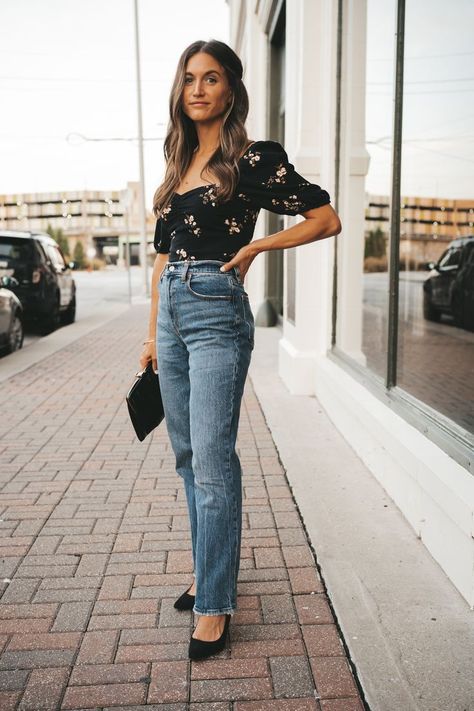 ashley wearing a black floral top, medium wash straight leg jeans, and black pumps holding a black clutch and standing on a sidewalk with red brick pavers next to the large window of a shop Black Jeans Outfit Summer, French Fall Outfits, Jeans Date Night Outfit, Fall Date Night Outfit, Statement Fashion Pieces, Fall Date Night, Straight Leg Jeans Outfits, Trendy Date Night Outfit, Outfits Jeans