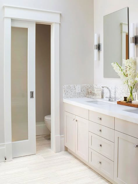 Calm & Comforting  One of the homeowner’s must-haves was a private toilet compartment, and with smart planning, they were able to incorporate one into this small 14x7-inch bathroom. The separate space includes extra towel storage, and the frosted-glass door admits light without sacrificing privacy. Floating mirrors flanked by linear sconces add to the room’s classic yet contemporary design. Makeover Kamar Mandi, Toilette Design, Double Sinks, Master Bath Ideas, Toilet Room, Ensuite Bathroom, Pocket Door, Master Bath Remodel, Bathroom Remodel Designs