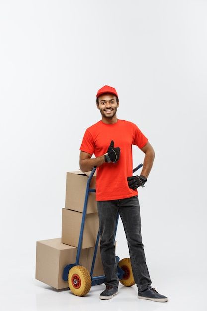 Free Photo | Delivery concept - portrait of handsome african american delivery man or courier pushing hand truck with stack of boxes. isolated on grey studio background. copy space. Grey Studio, Delivery Guy, Truck Boxes, Hand Trucks, Studio Background, Orange Shirt, Delivery Man, Hd Images, Free Photo