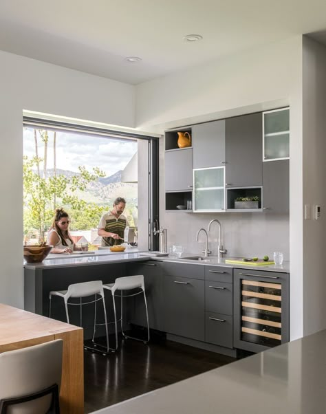 A pocket window in the kitchen allows for a double-sided bar area, with access to the outside grill. "It’s a great place to sit and drink your morning coffee and enjoy the views," said Goff, who placed two Tiffany counter stools at the pass-through bar. The kitchen cabinets are a mixture of rift-cut white oak and cabinets painted in Benjamin Moore’s low-gloss Iron Mountain hue, with Caesarstone countertops. Kitchen Pass Through Window, Pass Through Kitchen, Kitchen Window Bar, Kitchen Pass Through, Kitchen Pass, Pass Through Window, Kitchen Window Design, Target Kitchen, Window Bars