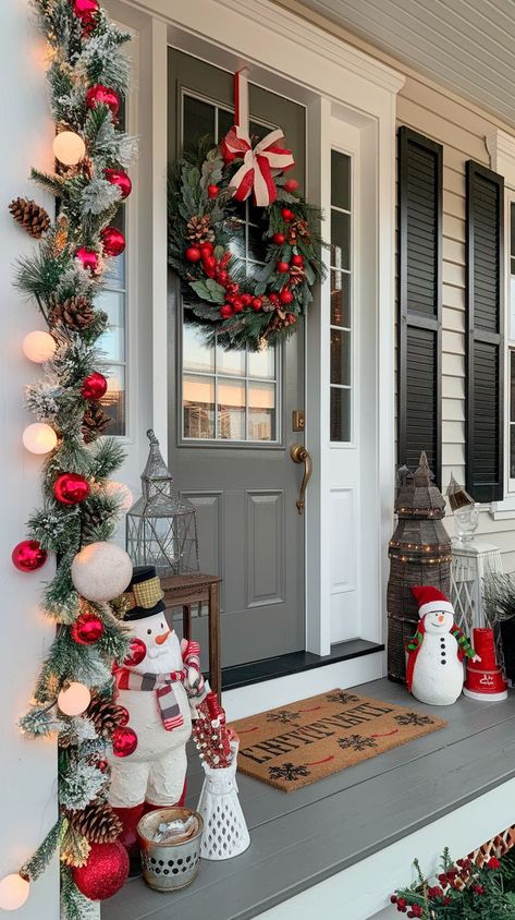 A cozy porch featuring a large red front door adorned with a festive green wreath. Lush garlands wrap around the doorframe, with twinkling white string lights and red bows. Red And White Christmas Porch Ideas, Exterior Xmas Decorations, Xmas Porch Decorating Ideas, Christmas Decor Ideas Red And White, Christmas Front Porch Decorating Ideas, Door Garland Christmas, Classic Christmas Decor Ideas, Red And Green Christmas Decor, Christmas Exterior