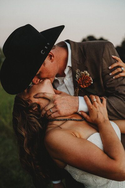 With hearts as adventurous as the rugged terrain surrounding them, Bailey & Derek embody the spirit of the West. The bride, radiant in a lace gown with sleeves paired with white short cowboy boots, exudes elegance with a touch of frontier grace. The groom, dashing in a tailored Western suit, completes the look with a cowboy hat and boots that echo the essence of a true Western gentleman. Cowboy Hat And Suit Wedding, Groom Wearing Hat, Western Wedding Mens Attire Groom And Groomsmen, Groom Suit Western, Mens Cowboy Wedding Attire, Groom In Hat, Spring Cowboy Wedding, Groom With Cowboy Boots, Cowboy Wedding Groom