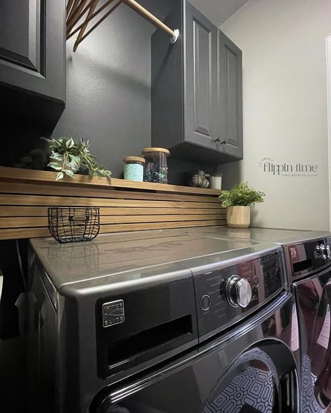 Incredible transformation in just two days! The decision to paint the walls ‘Iron Ore’ from @sherwinwilliams was spot on—it adds a dramatic and modern vibe. The sleek wood slat panel is a perfect way to hide the washer and dryer hookups, and it complements the bold geometric flooring perfectly. This laundry room makeover is seriously one of my favorites. #LaundryRoomMakeover #HomeTransformation #IronOre #SherwinWilliams #ModernDesign #DIYHome #InteriorInspo #LaundryRoomGoals #furnitureartis... Hide Water Lines In Laundry Room, Small Laundry Room Dark Paint, Dark Laundry Cabinets, Wood Cover For Washer And Dryer, Laundry Room Ideas Black Appliances, Hiding Water Lines In Laundry Room, Laundry Room Hookup Cover, Shelf Above Washer And Dryer Ideas, Hiding Dryer Vent In Laundry Room