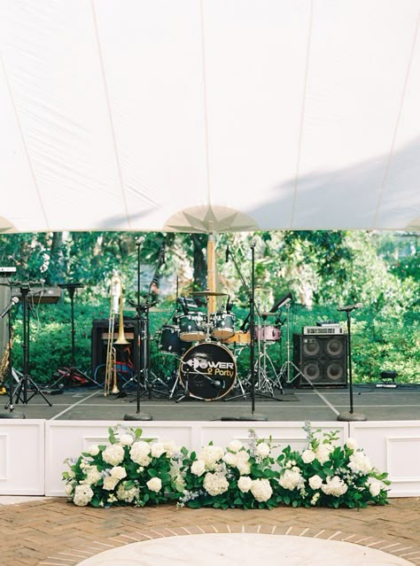 White stage wedding band set up with flowers. Power 2 Party wedding band. Charleston wedding photographer. Flowers In Front Of Band Wedding, Stage Flowers Wedding, Wedding Stage Flowers, Wedding Live Band Set Up, Tent Wedding Florals, Band Stage Wedding Decor, Wedding Band Stage Decor, Stage Wedding, Band Stage