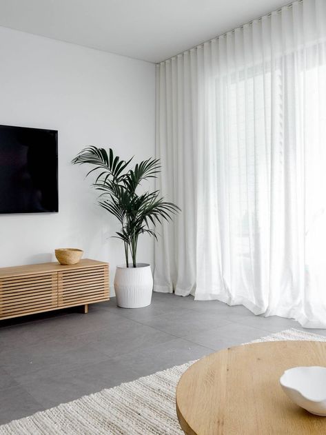 Dark and dull grey living area transformed into a warm and inviting space. The white linen sher curtains, oak side table, seagrass pouf, soft ivory rug, oak entertainment unit and indoor palm tree balance the cold of the grey floor tiles. Click now to see more photos of this beautiful living room Grey Tiles Living Room, Grey Flooring Living Room, Sheers Curtains Living Room, Lounge Room Styling, Tiles Living Room, Grey Floor Tiles, Living Room Tiles, Living Room Decor Curtains, Room Tiles