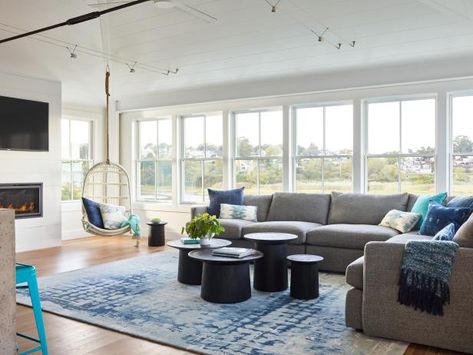 This room is all about the view, but in this small beach cottage, every inch counts. Designers decided to go with an extra long sectional (for the sitting space) and a fun hanging chair in the corner. The rest of the floor plan was kept open so that people can be sitting at the many turquoise stools at the island as well as the living space without additional furniture in between.  A fun assortment of various sized tables is an uncluttered look. See more at HGTV.com Corner Window Seats, Living Room Cottagecore, Small Beach Cottages, Small Beach Cottage, Monochromatic Living Room, Eclectic Coastal, Classic Living Room Design, Fish Shack, Beach House Decor Coastal Style