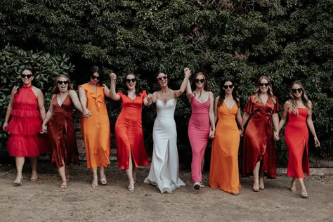 Bridal party in different pink, orange, rust and red bridesmaid dresses Mismatched Wedding Party Color Schemes, Red Mismatched Bridesmaid Dresses, Red Bridesmaid Dresses Mismatched, Red Orange Bridesmaid Dresses, Orange And Pink Bridesmaid Dresses, Pink And Orange Bridesmaid Dresses, Mismatched Red Bridesmaid Dresses, Pink Mismatched Bridesmaid Dresses, Sunset Bridesmaid Dresses